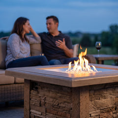 Sierra Square fire pit table at chat height with two people seated beyond it at dusk