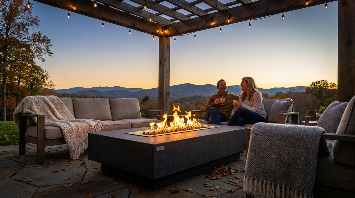 Couple relaxing beside an Elementi Hampton concrete gas fire pit table on a backyard patio at dusk